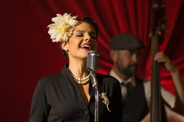 Professional jazz vocalist performing live at San Francisco corporate gala, wearing vintage-inspired attire with pearl necklace, singing into vintage microphone with band accompaniment, against red curtain backdrop and dramatic stage lighting